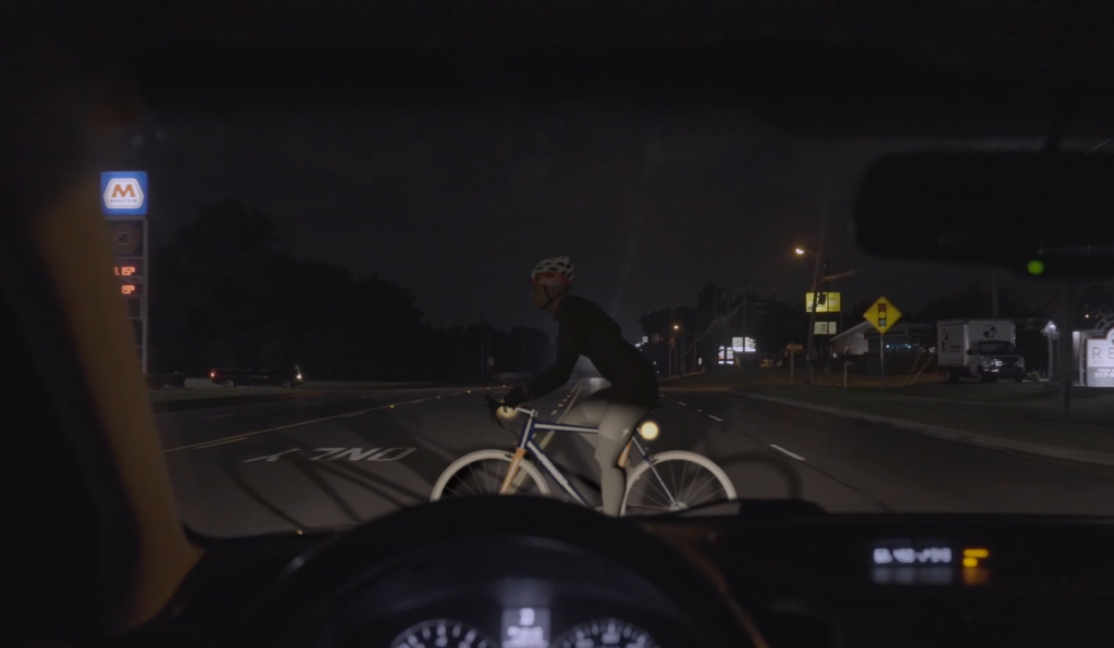 A biker in front of a car on a dark night